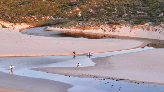 Surfers at sunset running across the river back to the carpark after catching waves.