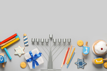 Hannukah composition with menorah, dreidels, gift box and rattle on grey background