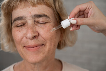Close-up portrait of an old woman applying hyaluronic acid serum with a pipette. Anti-aging face...