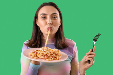 Young woman eating tasty pasta on green background, closeup