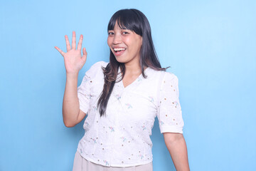Friendly Asian woman waving hand say hi or goodbye isolated blue background