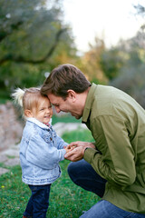Laughing dad with a little girl touching foreheads on a green meadow