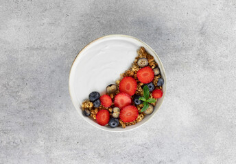 Yogurt bowl with granola and fresh berries: strawberries and blueberries on a gray background. Top view.