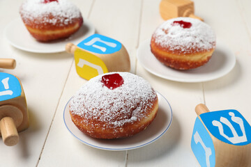Hanukkah composition with tasty donuts and dreidels on white wooden background, closeup