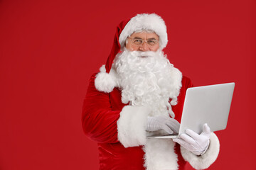 Santa Claus using laptop on red background