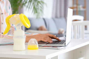 Breast pump with milk on table of working mother, closeup