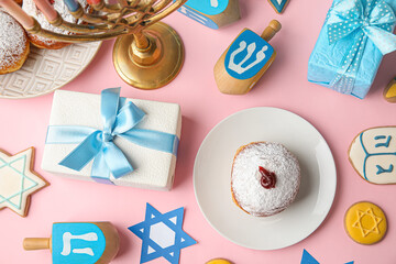 Dreidels, cookies, plate with donut and gift boxes for Hanukkah celebration on pink background
