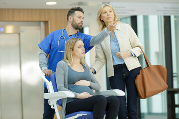 Obraz premium pregnant woman on wheelchair with doctor and mum in hospital