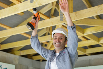 male builder using cordless drill on roof beam