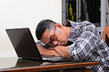 Adult Asian man sleeping in front of his laptop showing tiredness
