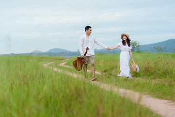 Obraz premium Asian man and woman couple walking in the middle of a meadow with a mountain background. morning sunlight