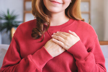 Closeup image of a happy young woman putting hands on her heart - obrazy, fototapety, plakaty