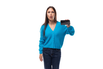 pretty young brunette woman dressed in blue v-neck cardigan demonstrates smartphone screen with...
