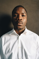 Close up portrait of young african man in white shirt against black wall in studio