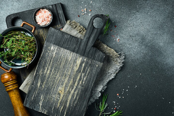 Wooden cutting board and spices, herb for food on black stone table. Menu, recipe mock up, banner background with copy space for text.