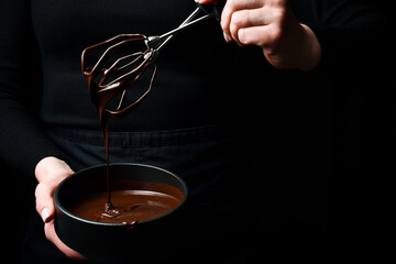Black bowl with dark hot chocolate in hands. Kitchen utensils. On a black background.