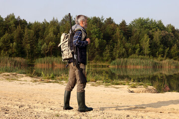 Naklejka premium Man with hunting rifle near lake outdoors. Space for text