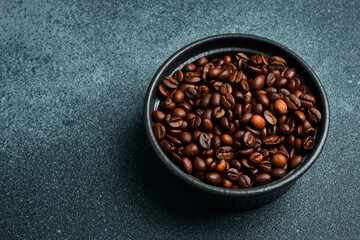 Roasted Arabica or Robusta coffee beans in a black bowl. Macro photo. Coffee background.