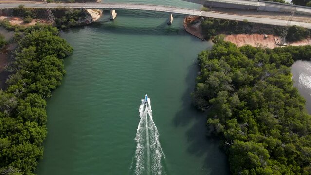 A speeding boat on an estuarine river seen from a bird's eye view speeding so fast going under two bridges also the drone reveals mangrove forests on both sides, Porlamar, Margarita Island, Venezuela.