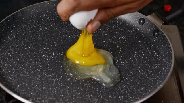 cracking an egg in the non stick fry pan, cooking sunny side up fried egg
