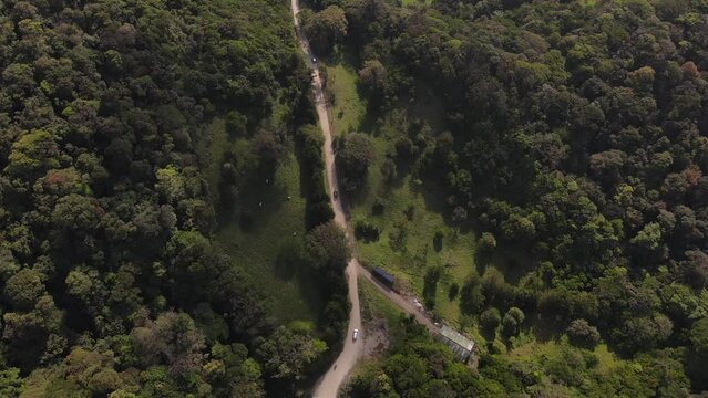 Slow-motion aerial drone footage of cars driving through a dirt road in a tropical rainforest rural landscape, in Monteverde, Costa Rica.