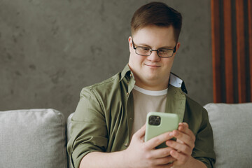 Young cool man with down syndrome wears glasses casual clothes use mobile cell phone sits on grey...