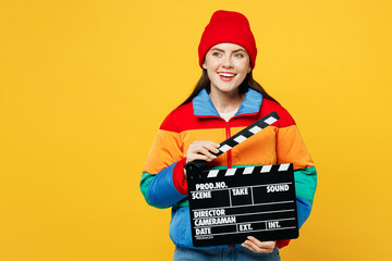 Full body young fun woman she wears padded windbreaker jacket red hat casual clothes hold in hand classic black film making clapperboard isolated on plain yellow background studio. Lifestyle concept.