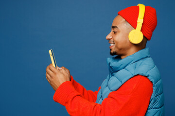 Young man of African American ethnicity wear padded vest red hat listen music in headphones use...