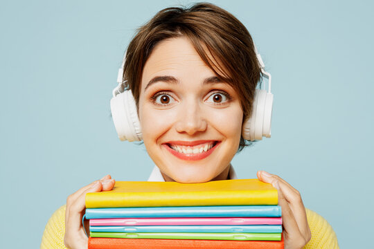 Close up young woman student wear casual clothes yellow sweater backpack bag hold books listen music in headphones look camera isolated on plain blue background High school university college concept