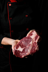 The chef is holding a ribeye beef steak. Aged and matured steak. Meat. On a black background.