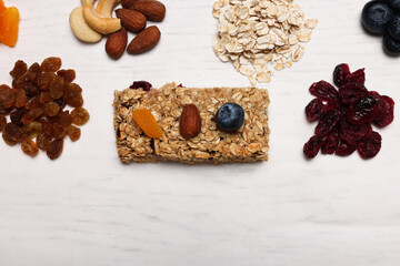 Tasty granola bar and ingredients on white wooden table, flat lay. Space for text