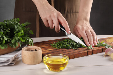 Woman cutting fresh parsley at white wooden table, closeup