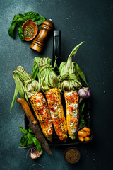 Grilled corn with spices and sauces on a black stone background. Barbecue. Organic food. Top view.