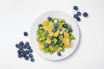 Plate of tasty fruit salad and blueberries on white background, flat lay