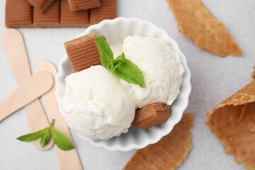 Scoops of tasty ice cream with mint leaves and caramel candies on white table, flat lay