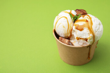 Scoops of tasty ice cream with mint, caramel sauce and candies in paper cup on green background. Space for text