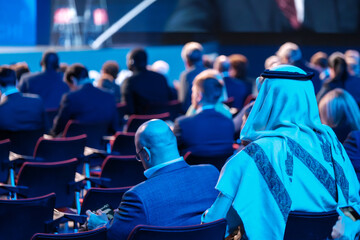 Back view of Arabian businessman attending global conference meeting in illuminated auditorium at...