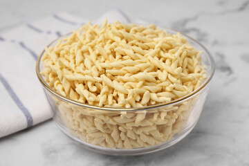 Uncooked trofie pasta in bowl on white marble table, closeup