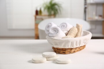 Fototapeta na wymiar Basket with spa herbal bags, towels and stones on white wooden table in bathroom, space for text