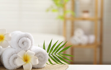 Fototapeta na wymiar Spa composition. Towels, plumeria flowers and palm leaves on white table in bathroom, space for text