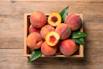 Cut and whole fresh ripe peaches with green leaves in crate on wooden table, top view