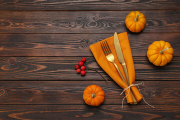 Cutlery, napkin and pumpkins on wooden background, flat lay with space for text. Table setting