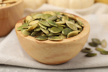 Wooden bowl with pumpkin seeds on table, closeup