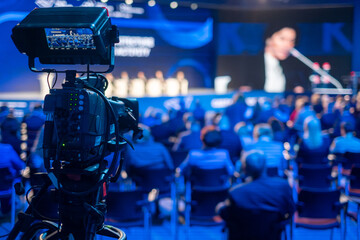 Video camera capturing global business conference in illuminated blue auditorium at export forum - obrazy, fototapety, plakaty