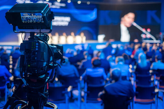 Video camera capturing global business conference in illuminated blue auditorium at export forum