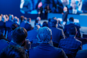 Businessmen listening to speaker giving presentation in illuminated auditorium at export forum 