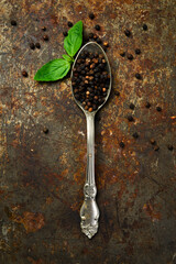 Fragrant black peppercorns in a metal spoon. Spices and condiments. Top view. On an old textured background.