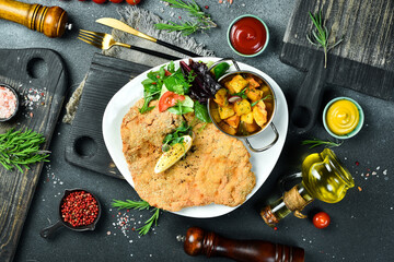 Large fried chicken schnitzel with vegetables. In a plate. On a black stone background. Photo of...