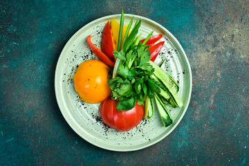 Cutting fresh vegetables: tomatoes, paprika, parsley, cilantro, onions. On a plate. On a dark stone...