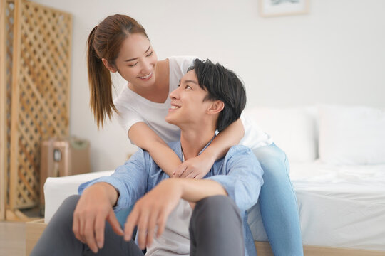 Asian young couple woman hugging man from behind  with positive emotion lover. Attractive Husband with Wife embracing spending time together at home. Relationship of feeling in love.